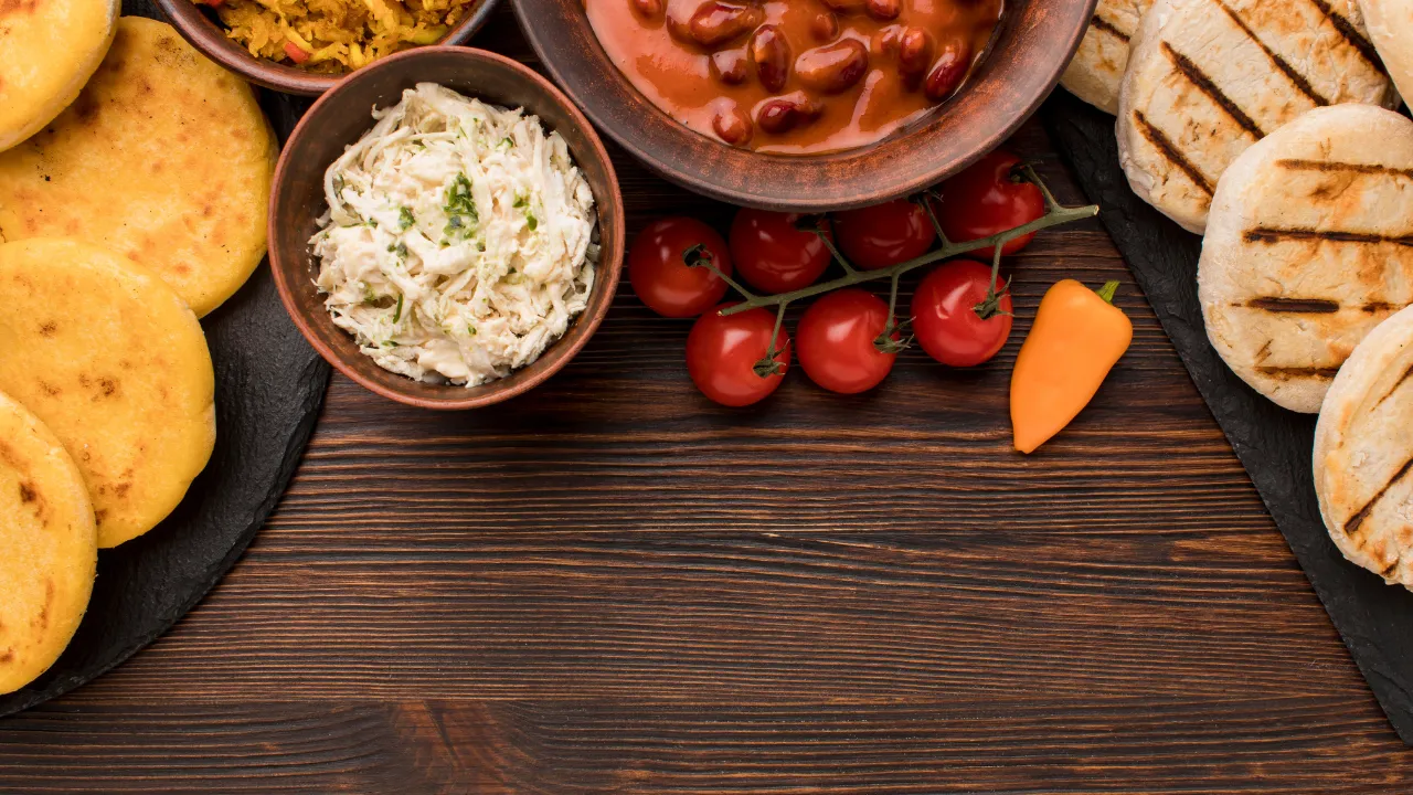 Mesa rústica com pratos típicos de comidas do sítio, incluindo pão caseiro grelhado, feijão, farofa, salada cremosa, tomates-cereja e bolinhos assados.